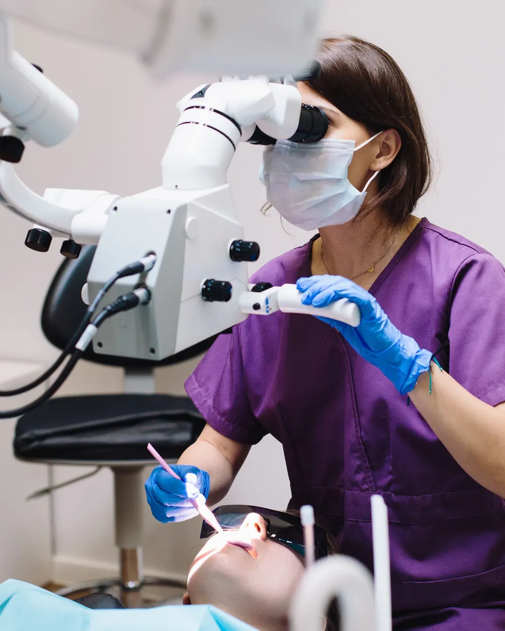 Dentystka pracująca przy mikroskopie zabiegowym nad leżącą pacjentką